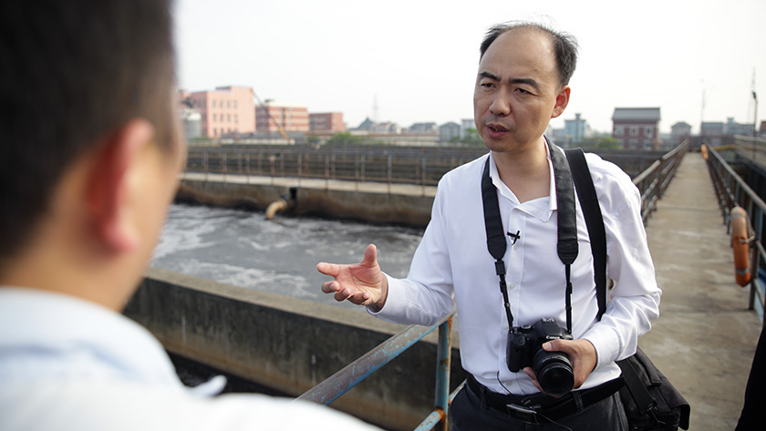 Ma Jun, IPE founder, inspecting a factory's wastewater stream in China. He wears a camera around his neck. 