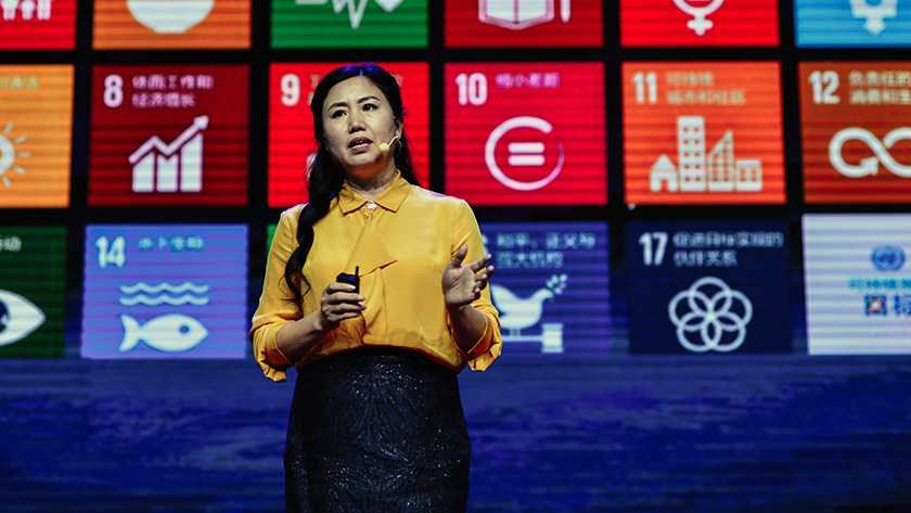 A speaker presenting on the main stage at TEDxChengdu Skoll in front of a projection of the icons for the Sustainable Development Goals