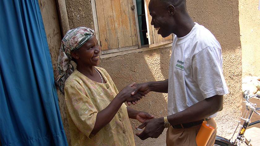 Francis, a Kampala, Uganda-based BasicNeeds volunteer making a home visit with a smiling woman in her doorway