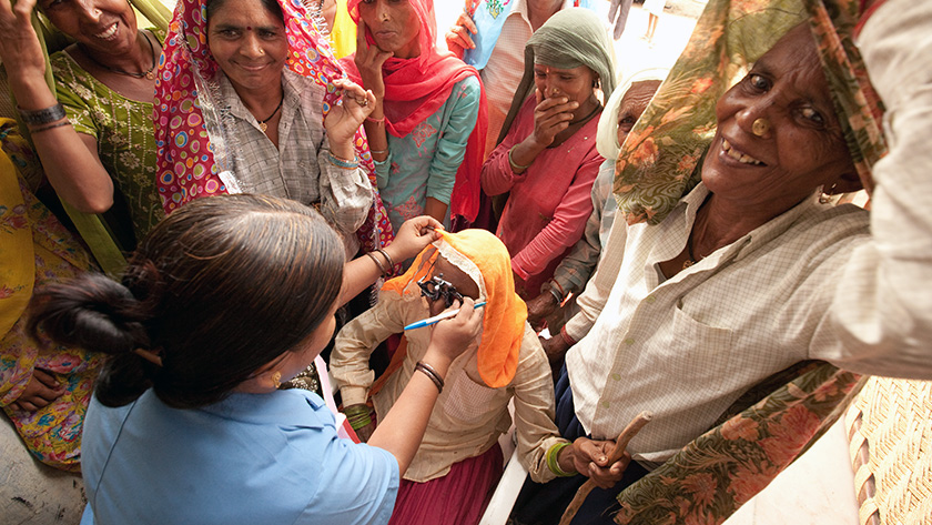 A woman in India getting prescriptions for glasses, surrounded by other smiling women
